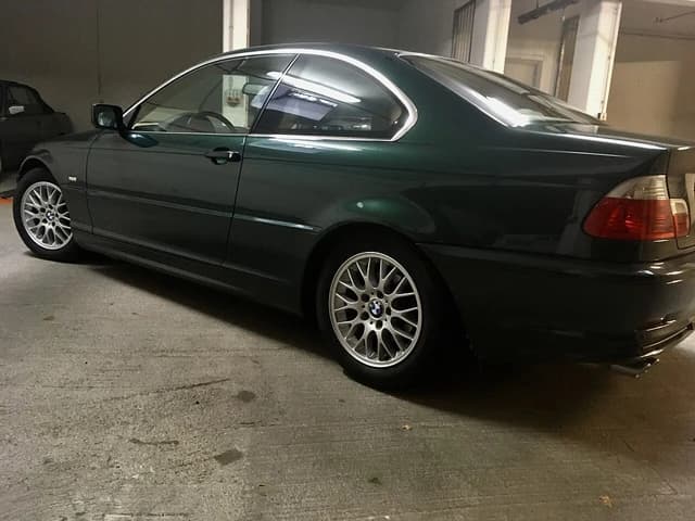 Dark green BMW E46 Coupe parked in an indoor garage, seen from the rear passenger side.