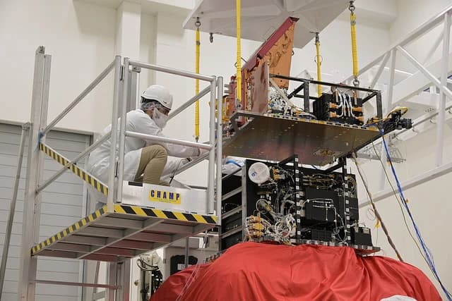 Engineer on a platform installing equipment on a space mission payload module.