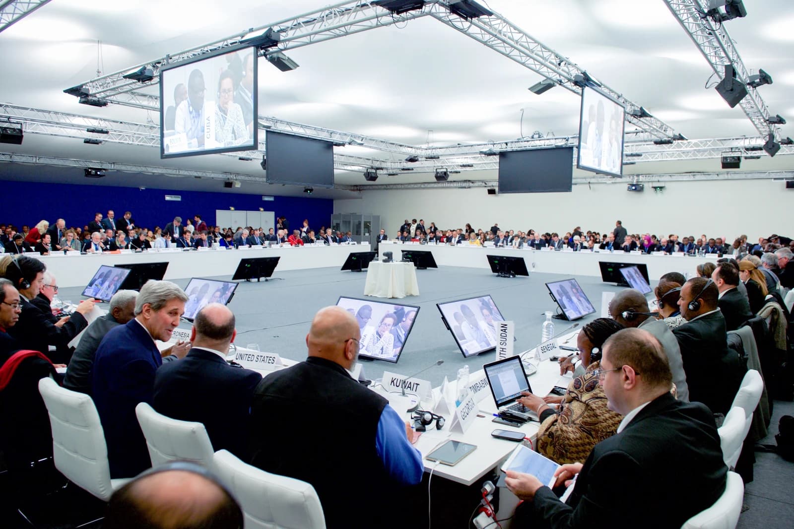 John Kerry, Secretary of State, seated at a table during a conference plenary session.