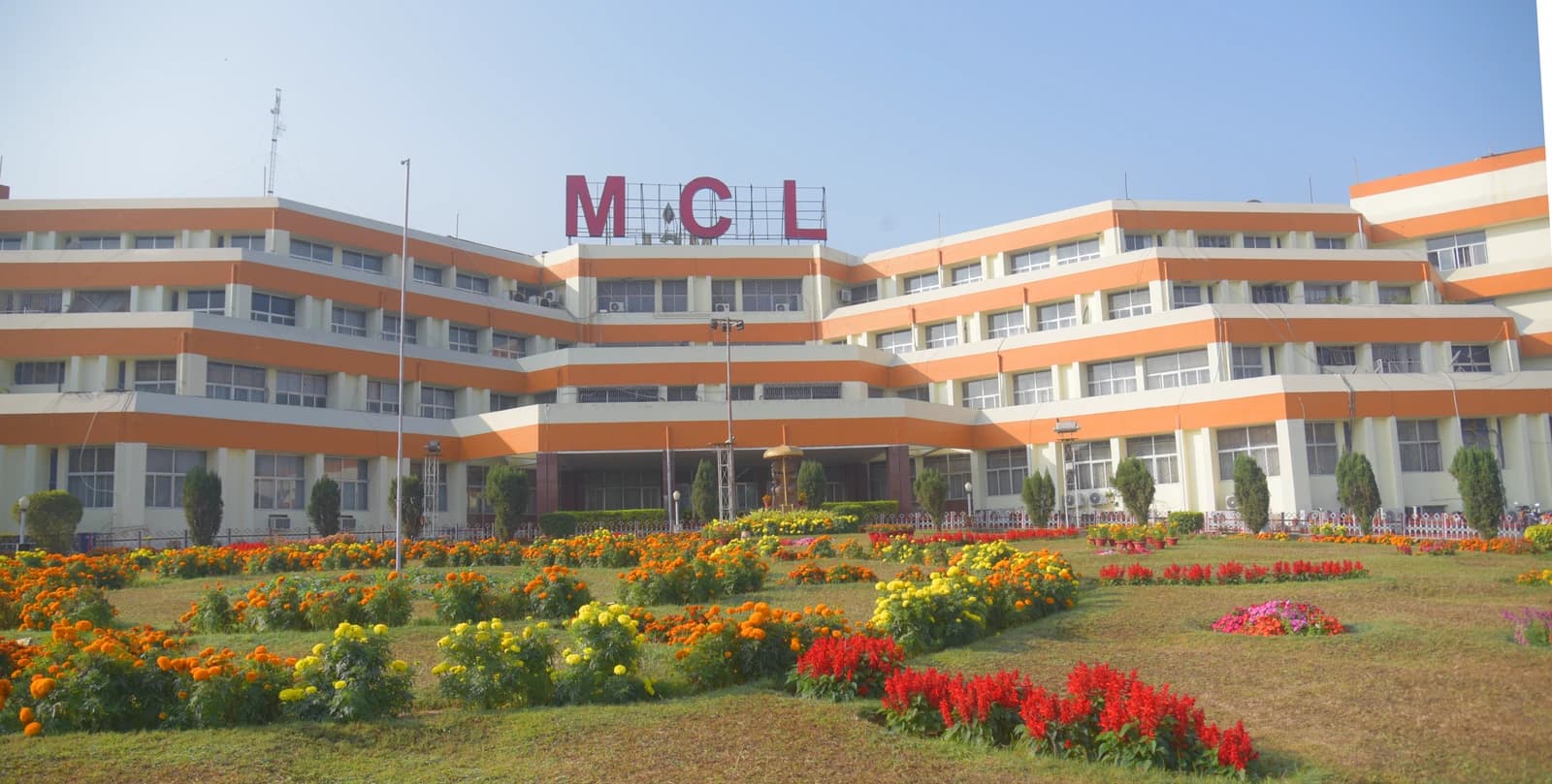 Mahanadi Coalfields Limited building with large MCL sign on roof, surrounded by flowering gardens.