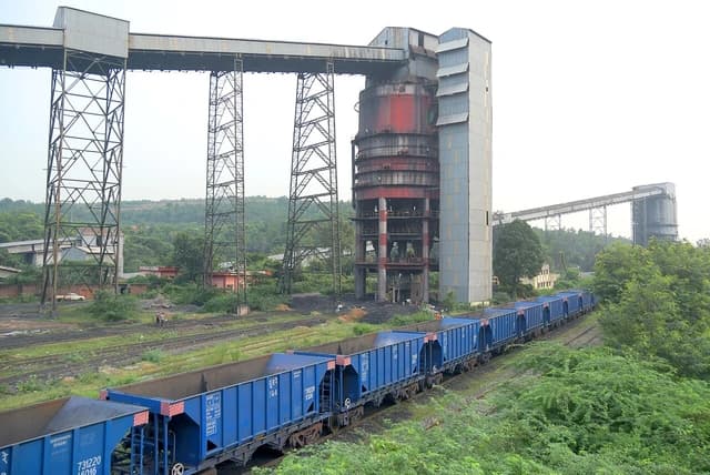 Coal handling plant structure with multiple conveyor belts and a long blue train.
