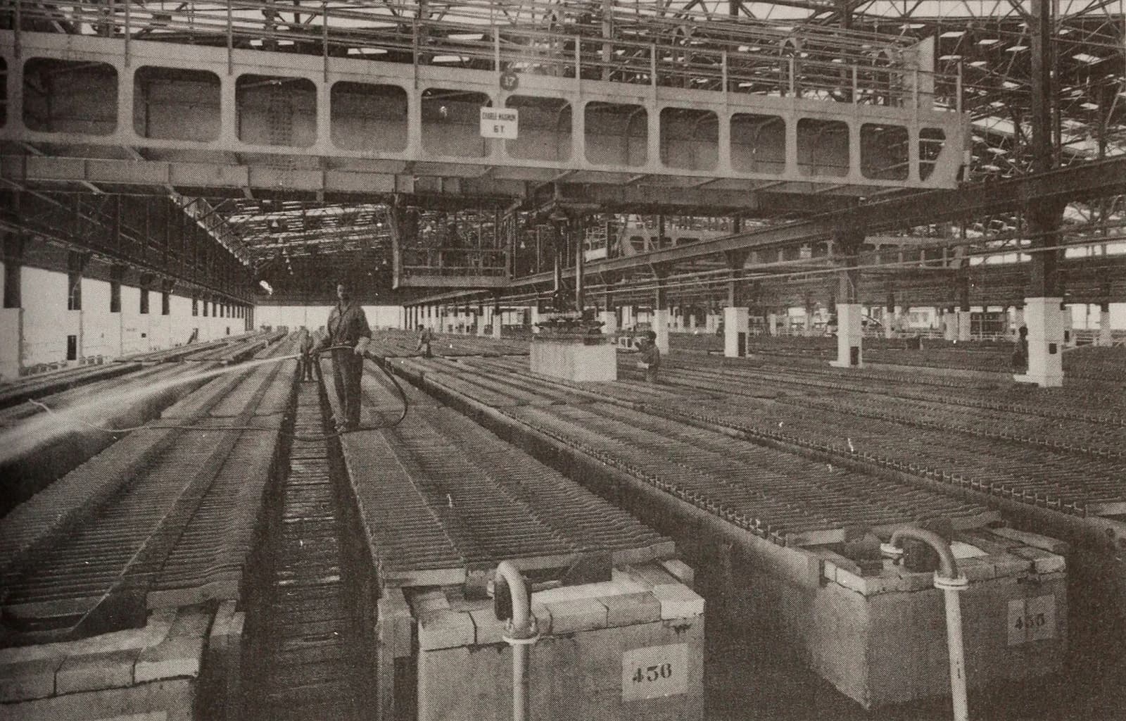 A worker hosing down copper electrolysis tanks inside a large industrial facility.