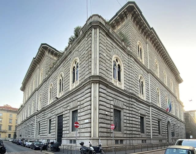 Exterior view of a large, stone building with arched windows in Milan, Italy.