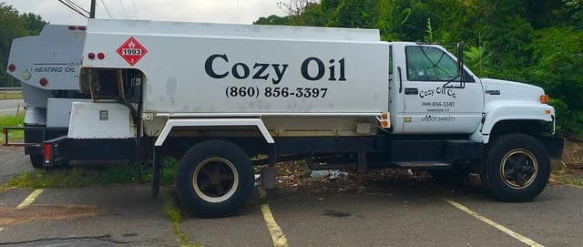 White heating oil delivery truck from Cozy Oil Co. parked on asphalt.