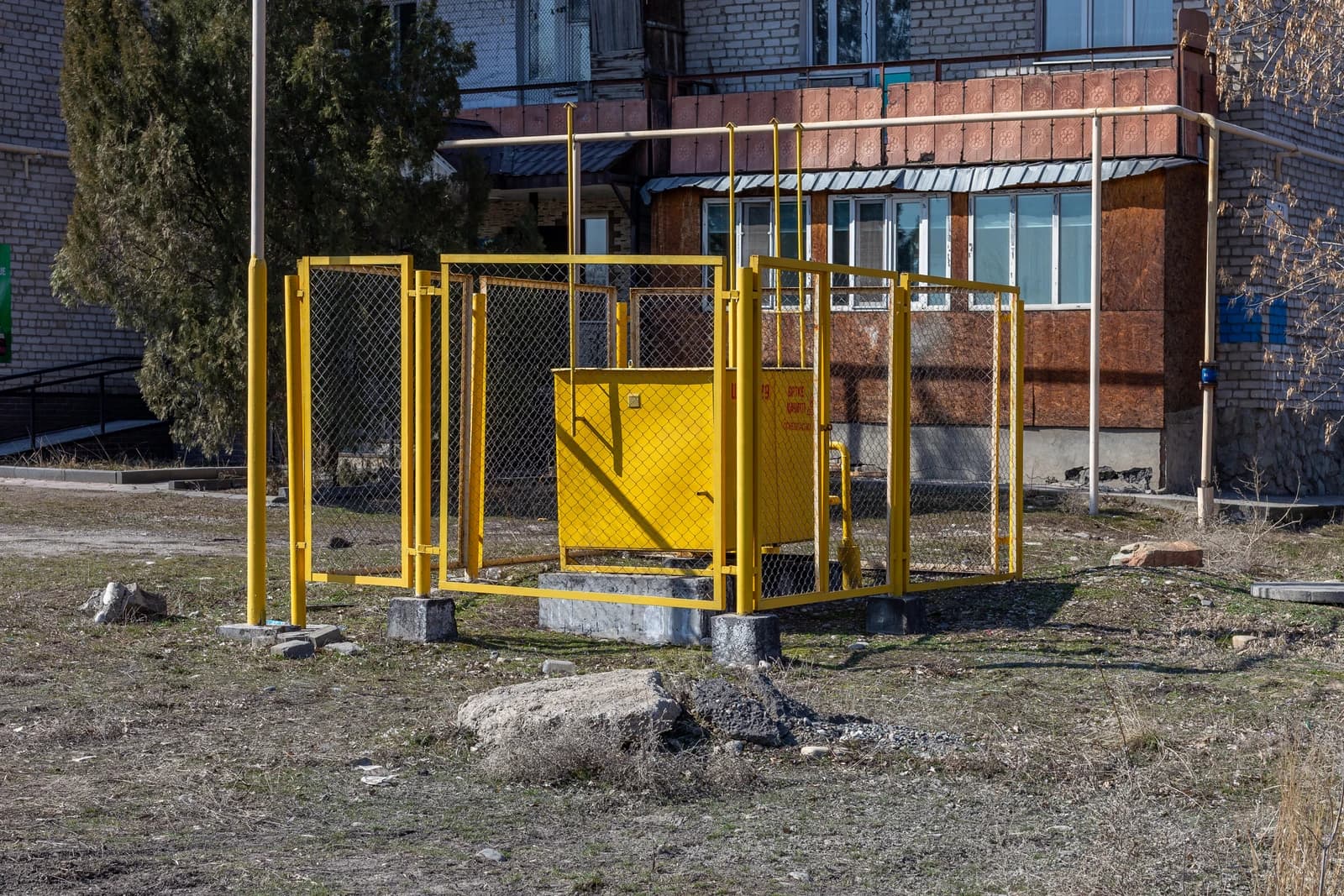 Yellow gas distribution point enclosed by a fence next to a building.