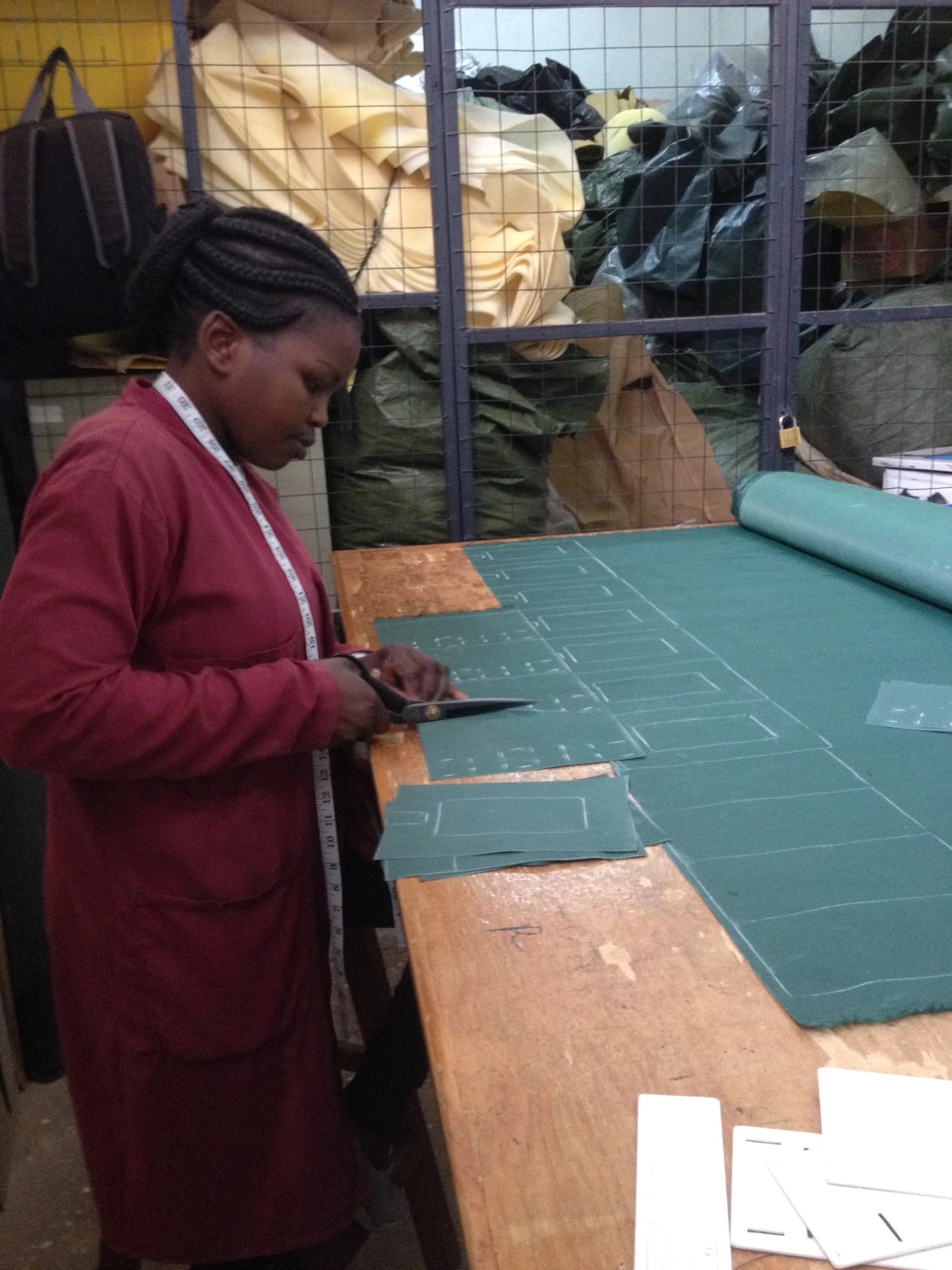 A person is cutting green fabric on a large wooden table in a workshop.