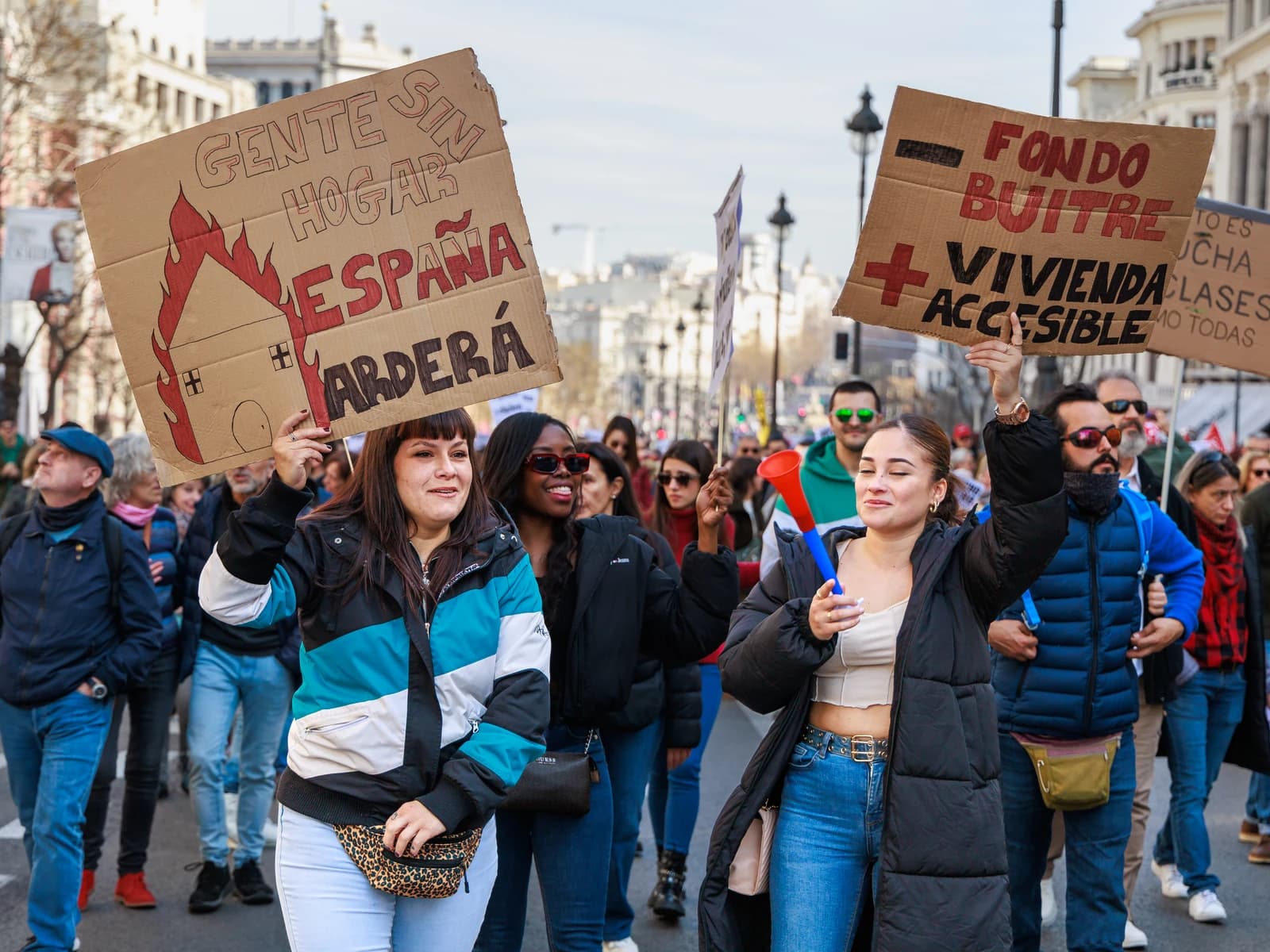 Housing activists protest against real estate practices in Madrid, holding signs.