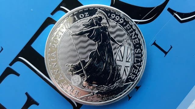 A 2021 British Britannia 1 ounce silver coin rests on a blue surface.
