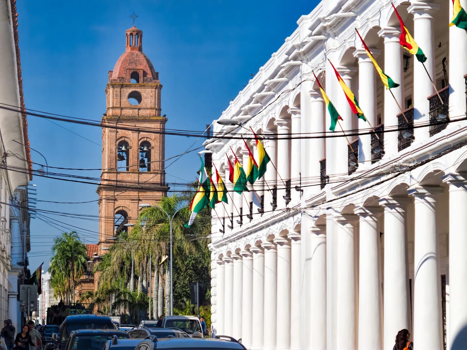 A brick bell tower rises above buildings adorned with Bolivian flags in Santa Cruz.