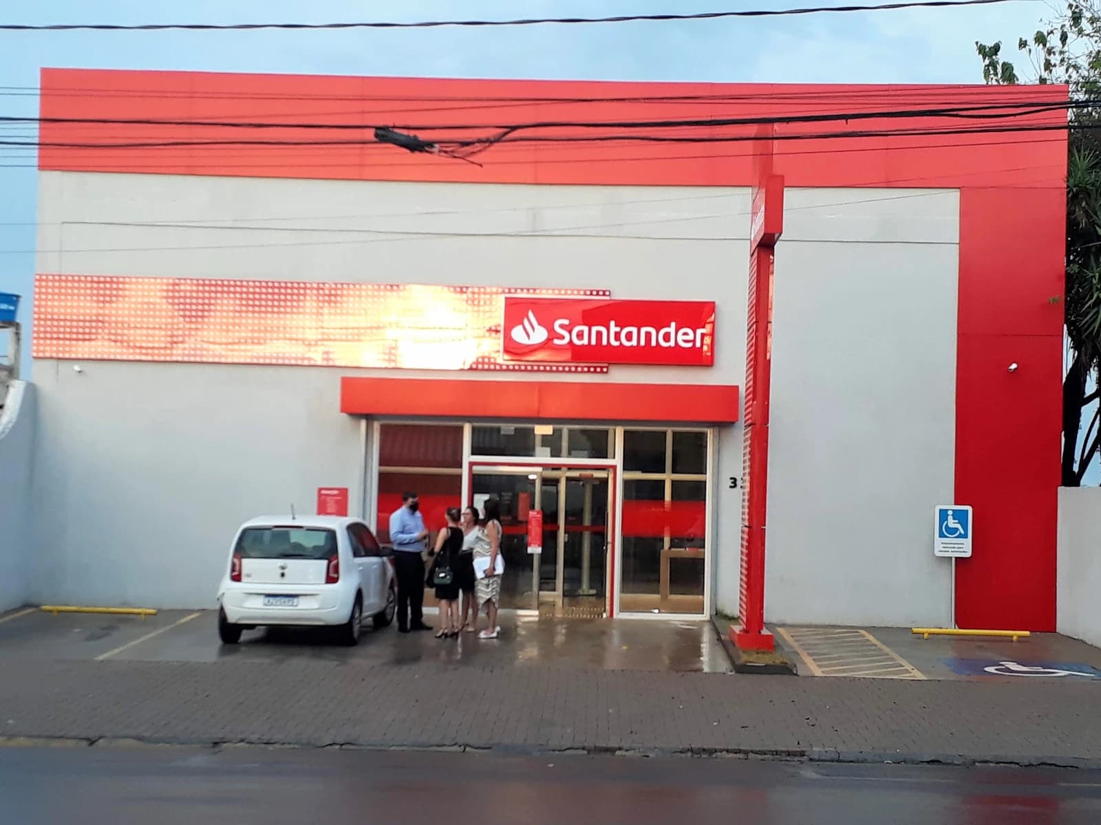 Exterior view of a red and grey Santander bank branch with people entering.