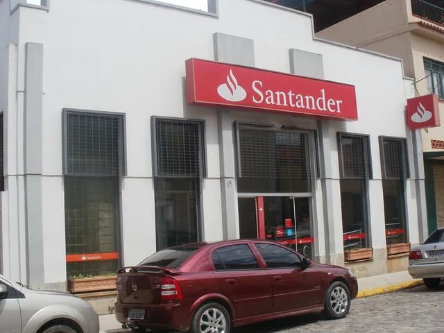 Exterior of a Santander bank branch with a red sign, cars parked on the street.