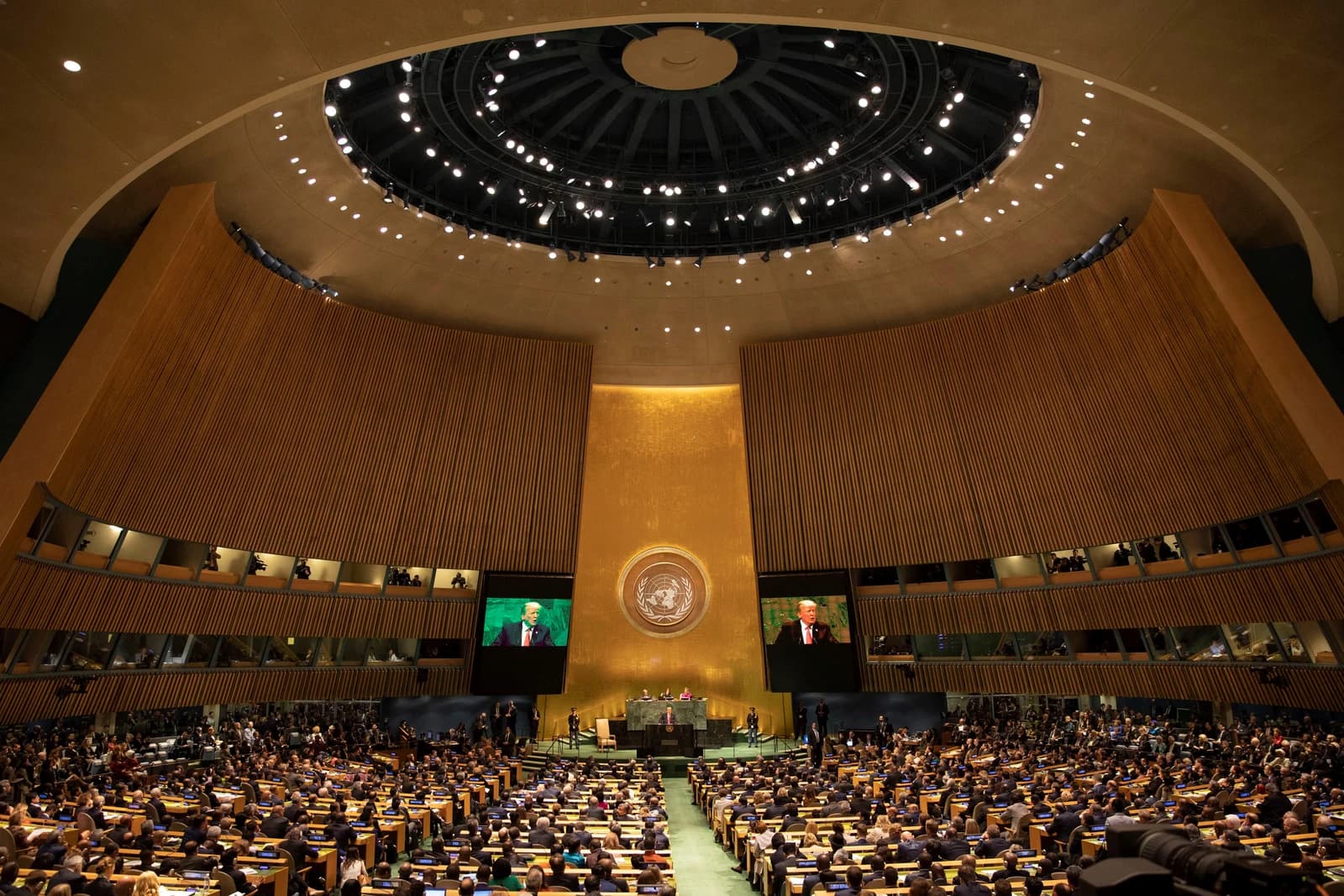 President Donald Trump speaking on large screens in the United Nations General Assembly hall.