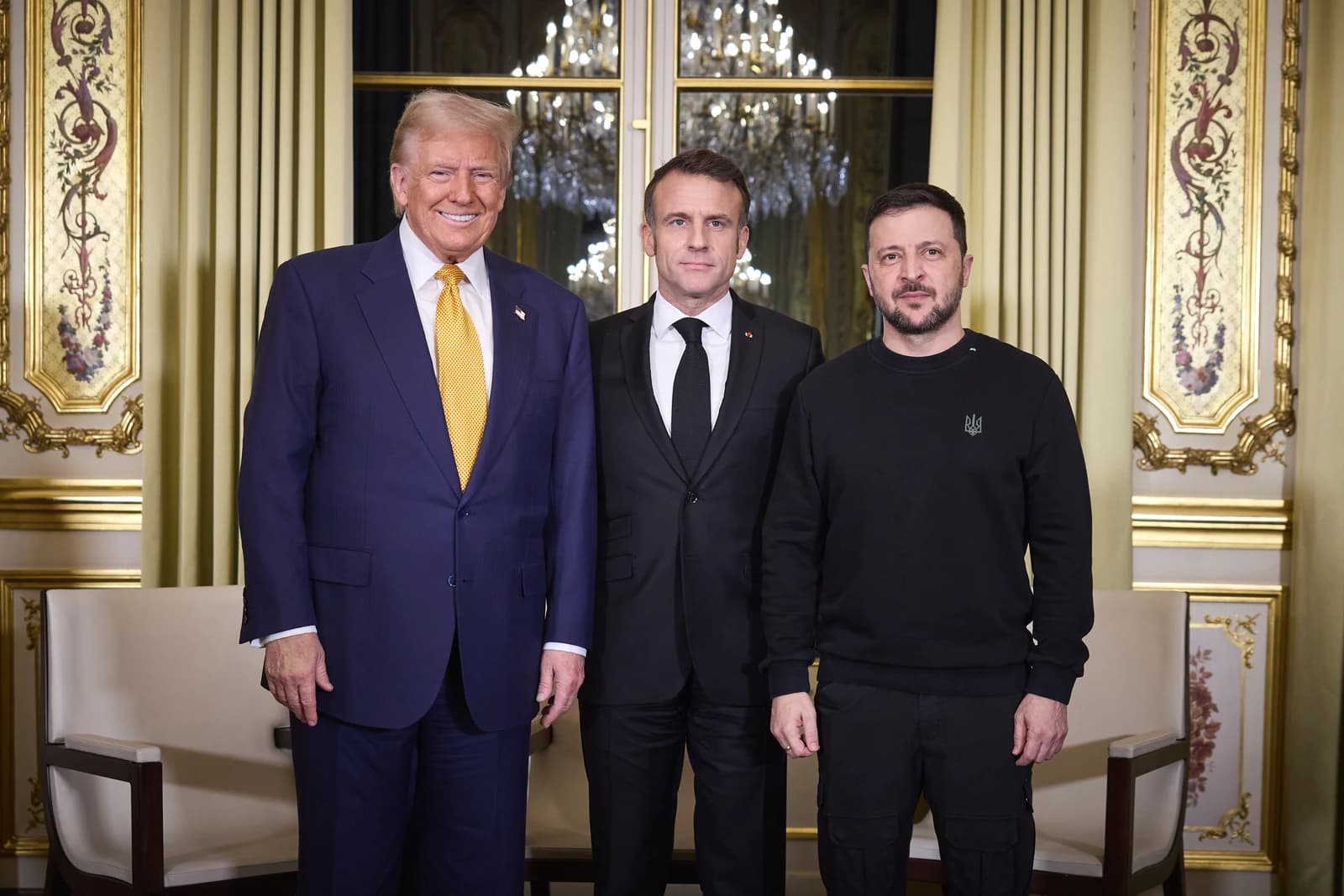 Donald Trump, Emmanuel Macron, and Volodymyr Zelenskyy standing together indoors.