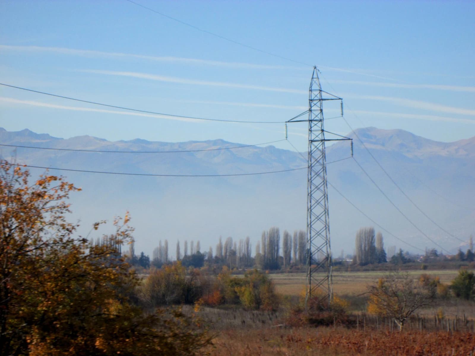 An electricity transmission tower stands in a field with power lines extending across the frame.