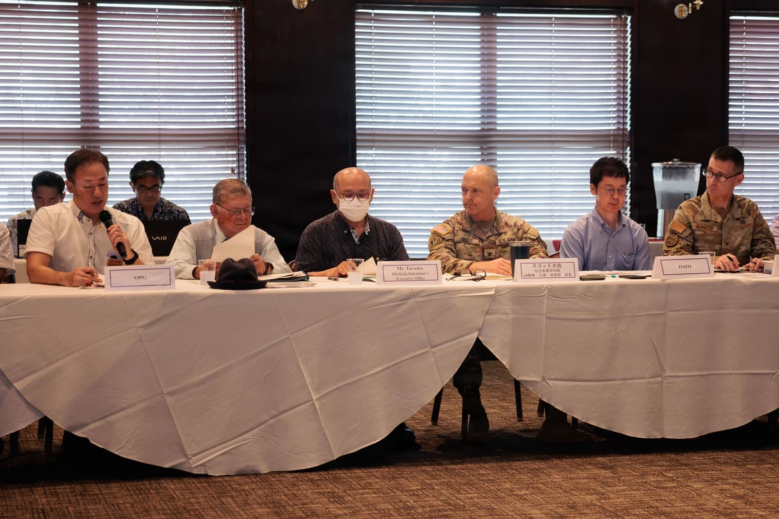 Attendees, including military personnel and civilians, seated at a long table at a community forum.