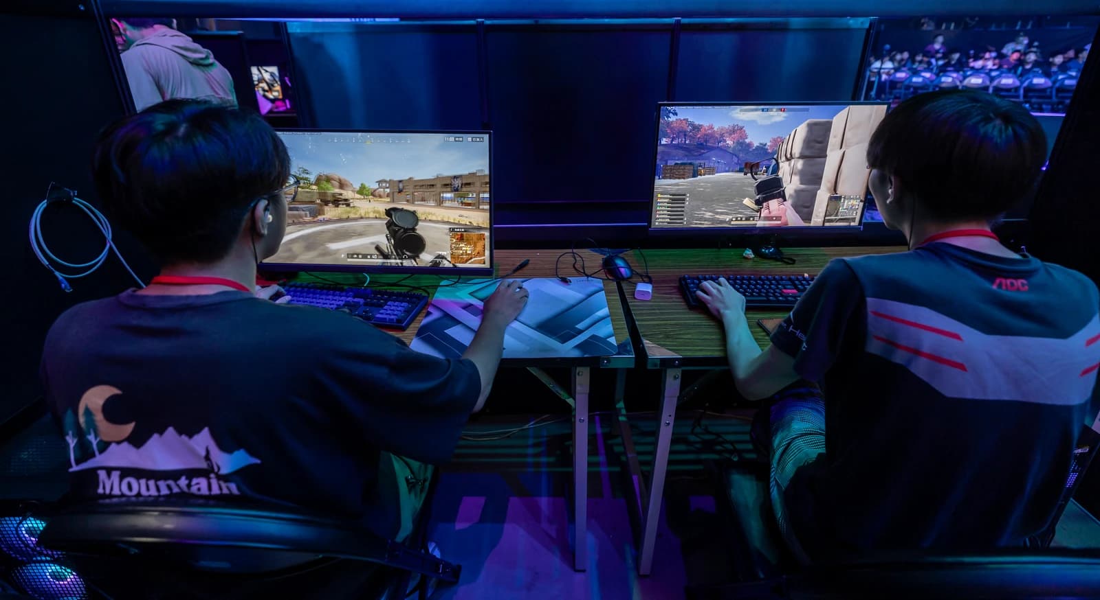 Gamers play video games on monitors at a brightly lit esports event.