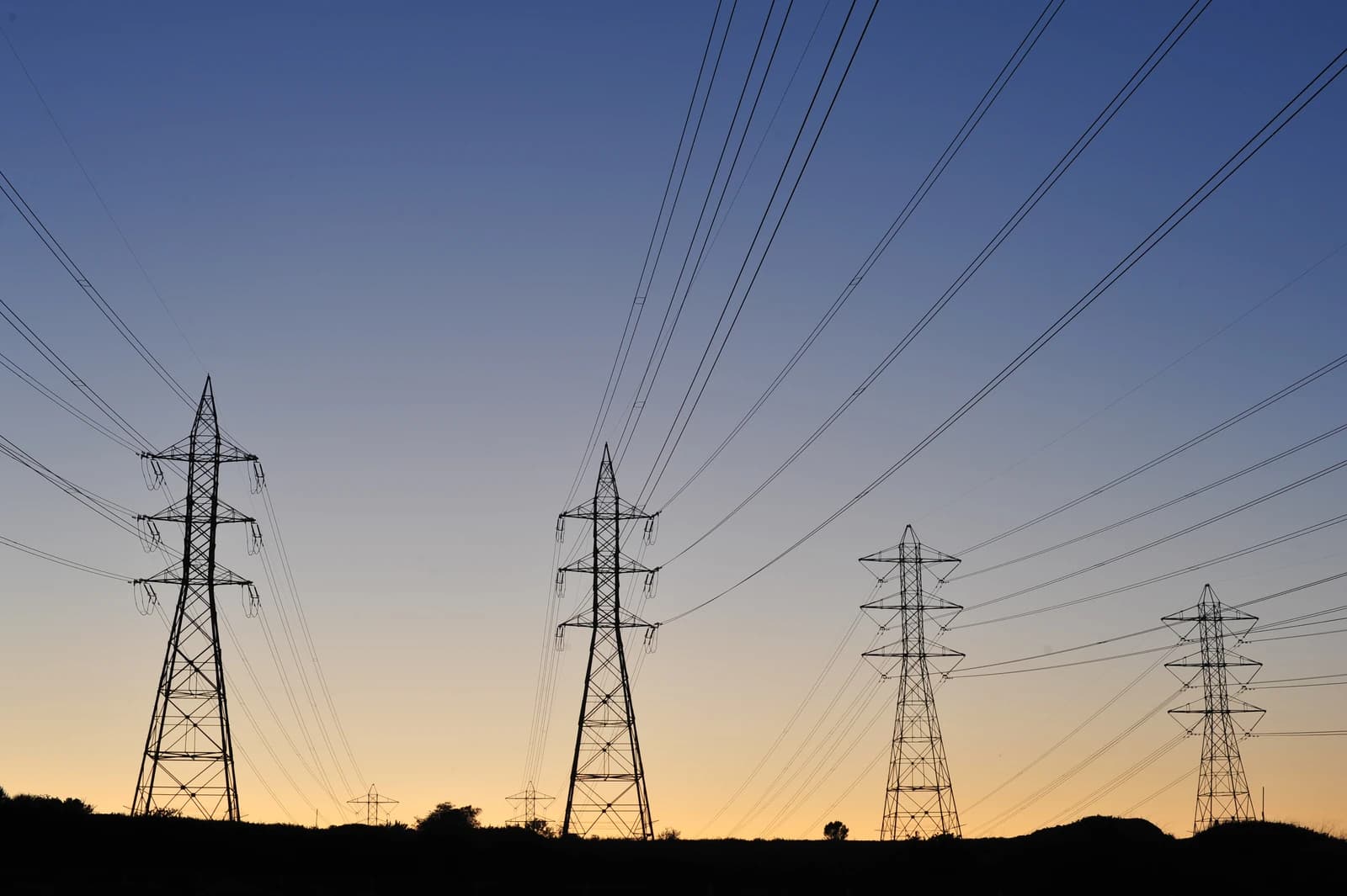Multiple electricity transmission towers silhouetted against a colorful sunset sky.