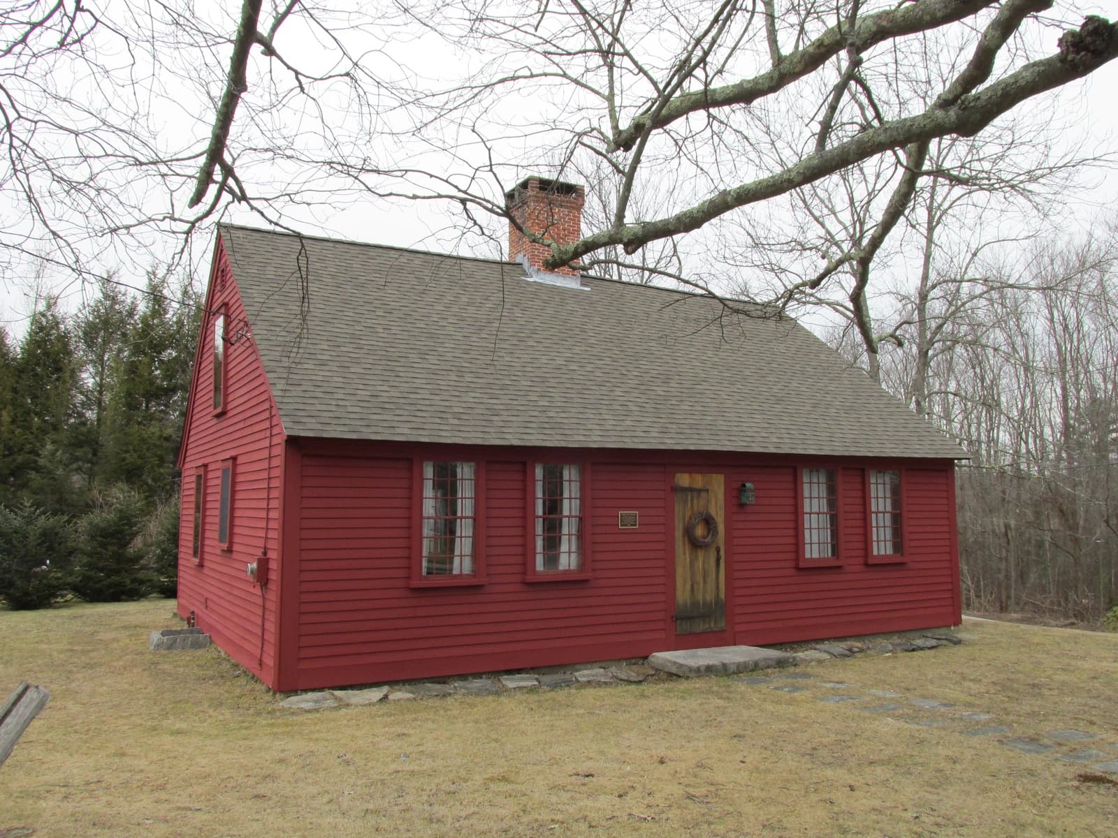 Red-painted colonial house with a shingle roof and bare trees surrounding it in Burrillville, Rhode Island.