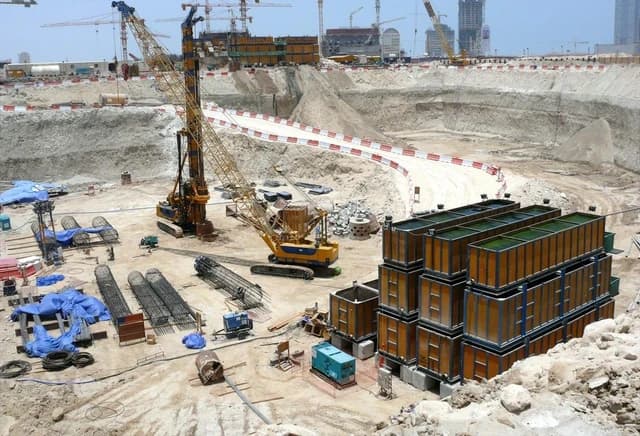 Burj Al Alam building under construction in Dubai with cranes and materials in an excavated pit.
