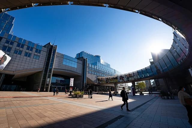 People walk on a sunny day outside the European Parliament building in Brussels.
