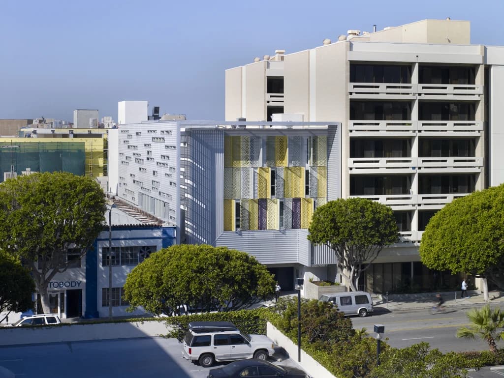 Modern multi-story building with colorful facade screens next to a larger, older building.