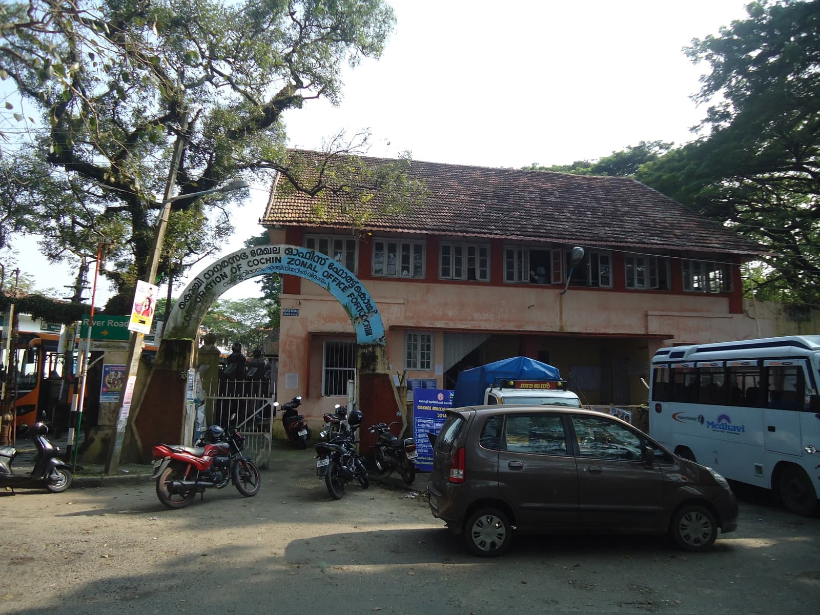 Kochi Corporation Zonal Office Fort Kochi building with an arched entrance and parked vehicles.