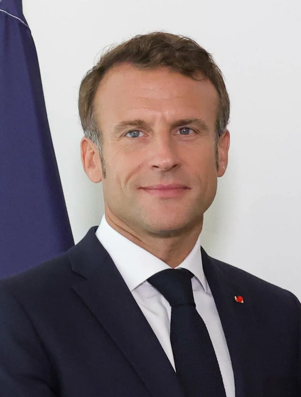 Emmanuel Macron, President of France, poses for a portrait against a white background with a blue flag.