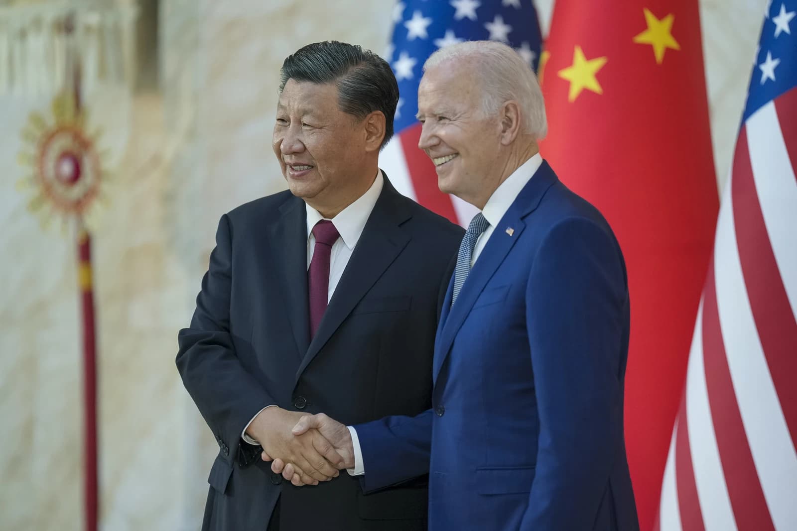 President Joe Biden and President Xi Jinping shaking hands, with US and Chinese flags behind them.