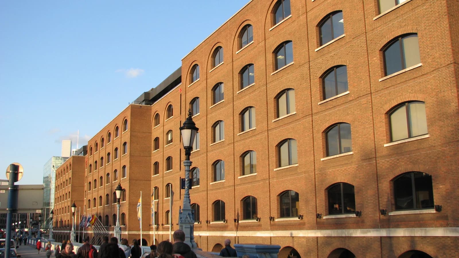Brick building with arched windows, light blue sky above, people walk below.