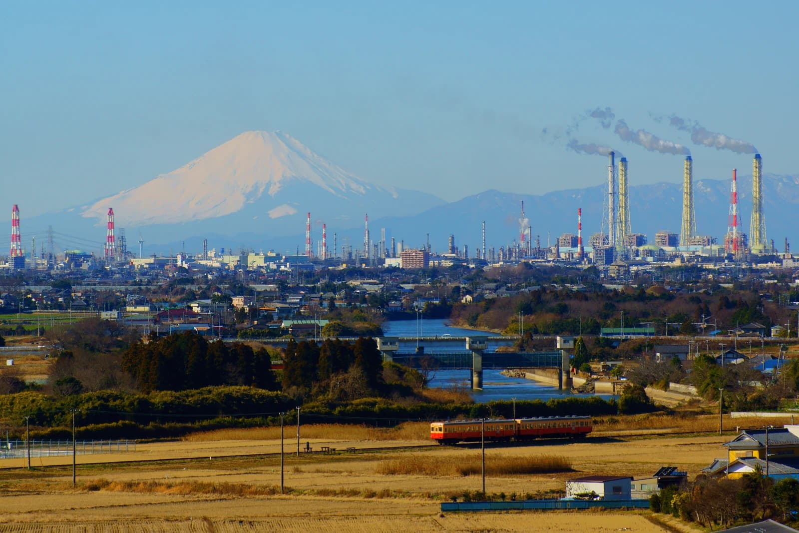 Mount Fuji in background of industrial petrochemical complex with smoking chimneys.