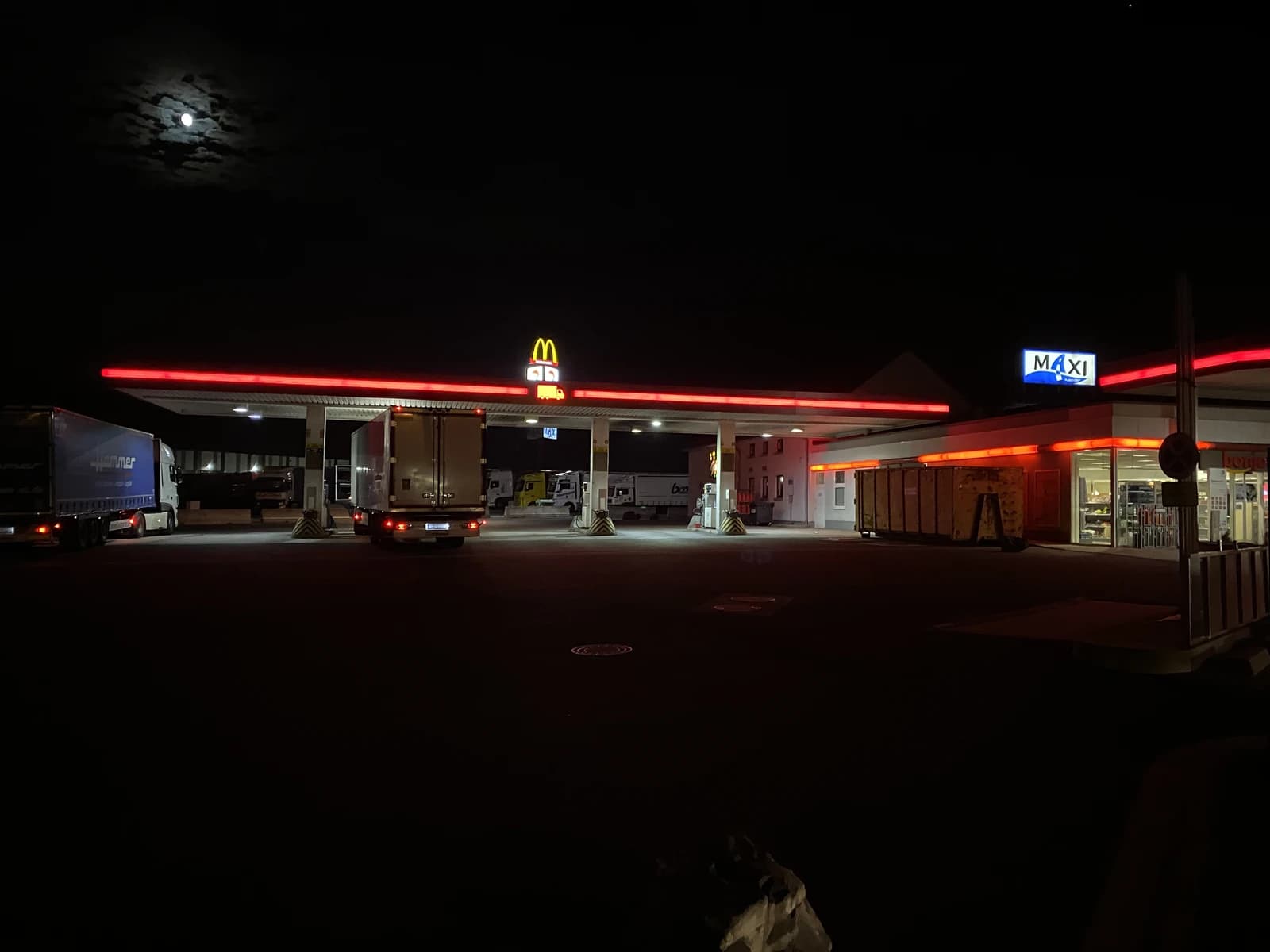 Trucks parked at a gas station and truck stop in Kirchheim, Germany, at night.