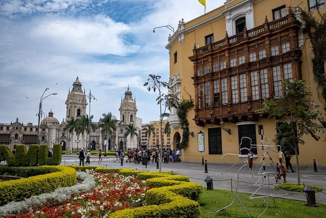 People walk through the historic center of Lima, Peru, with colonial buildings and landscaping.