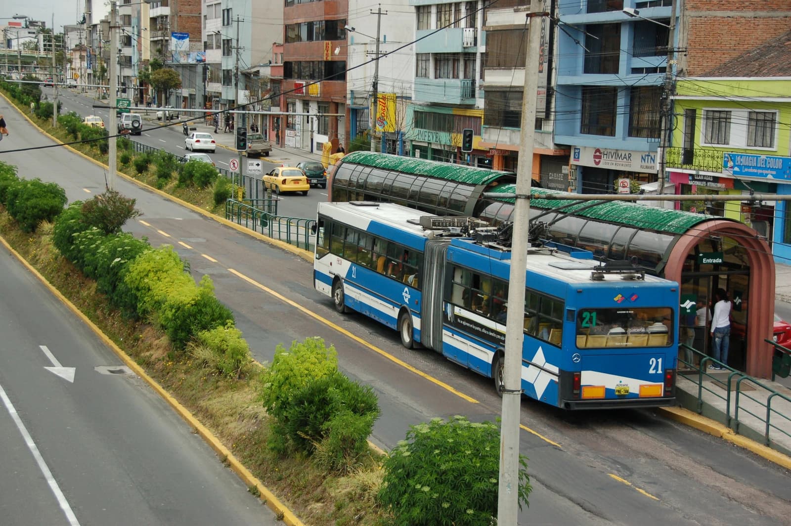 Blue and white articulated trolleybus at a bus stop in Quito, Ecuador.