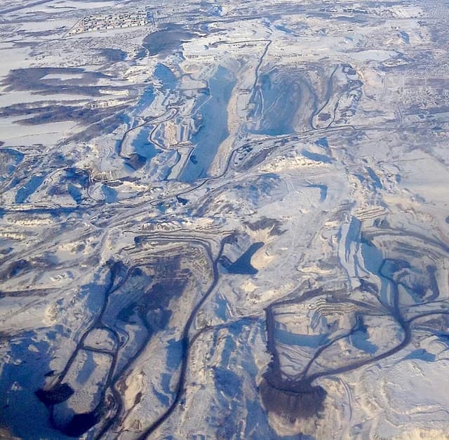 Aerial view of a vast open-pit coal mine in a snow-covered landscape.