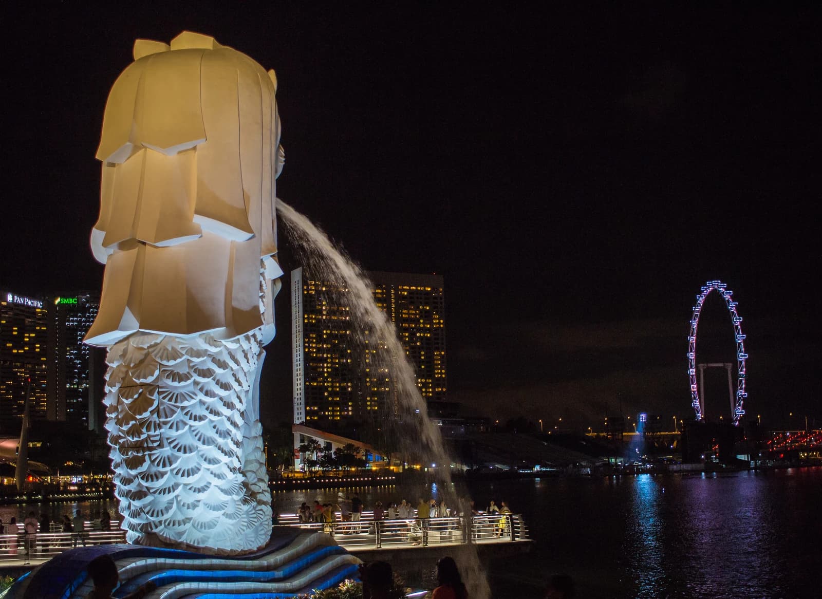The Merlion, a statue with a lion's head and fish's body, spouting water into a bay at night.