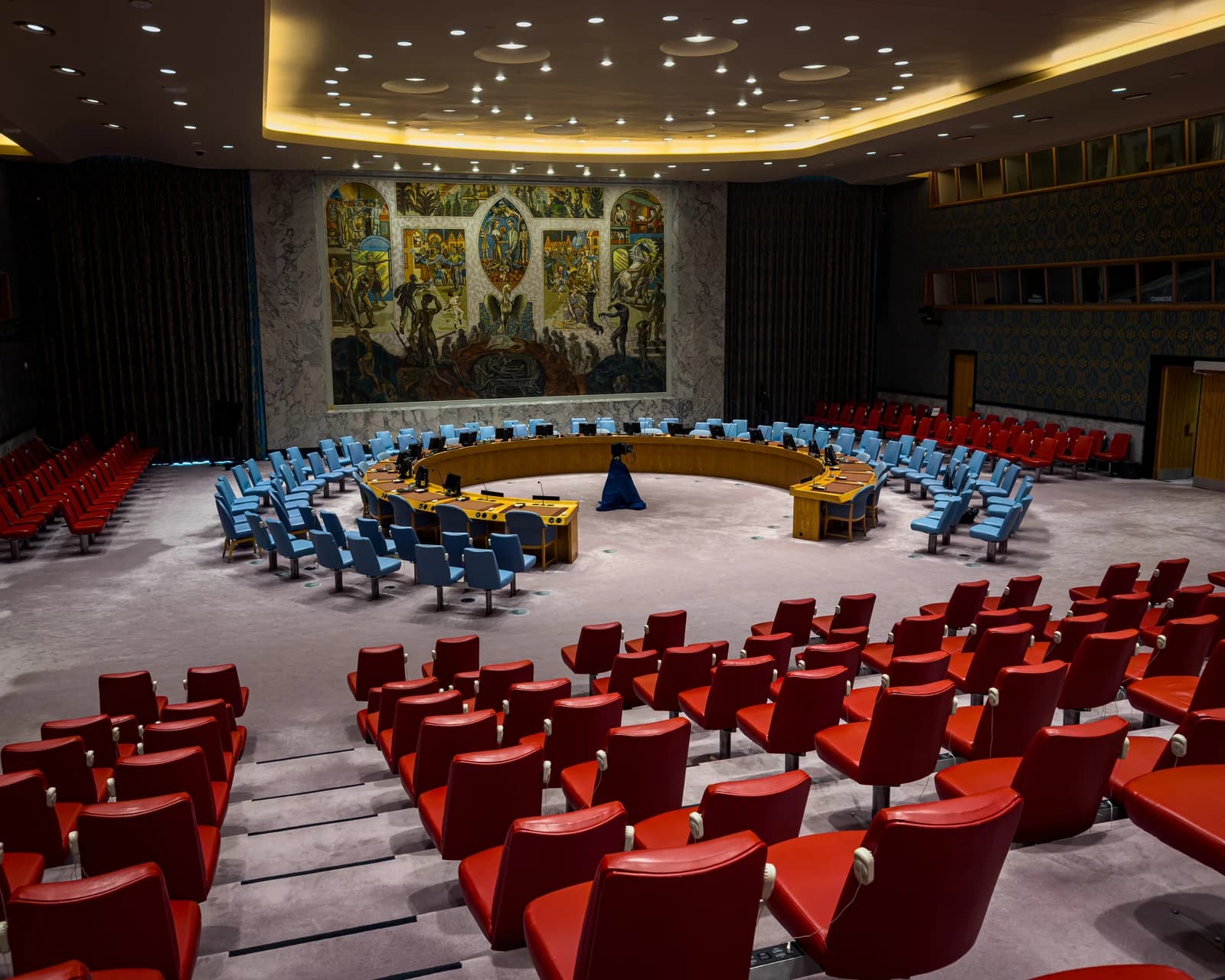 The United Nations Security Council chamber with empty seats and a large mural on the wall.