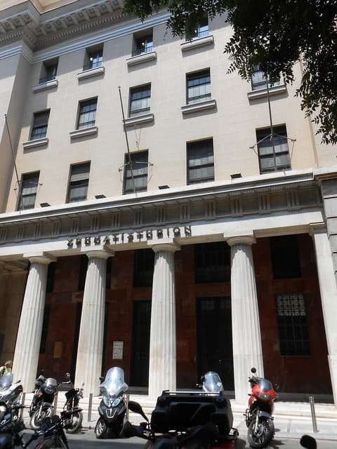 Exterior view of the Old Athens Stock Exchange building with columns and parked motorbikes.