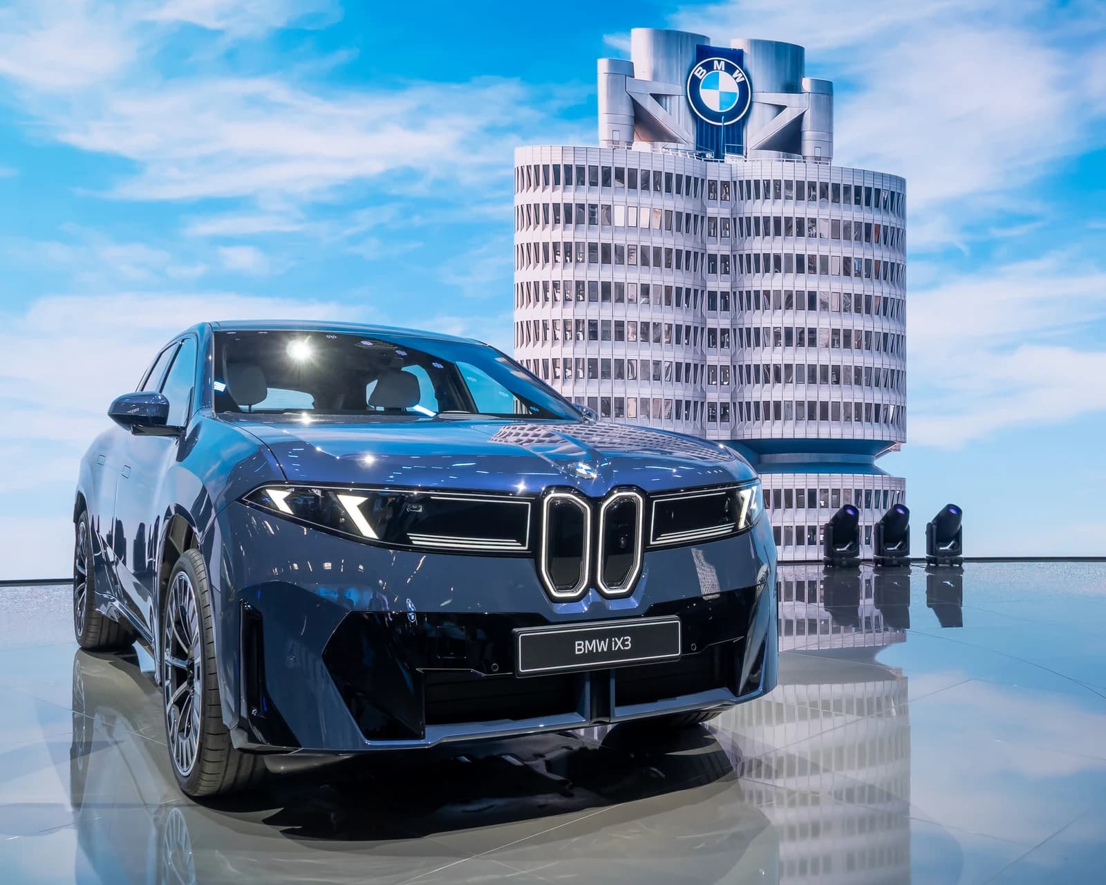A dark blue BMW iX3 electric SUV on display with the BMW building in the background.