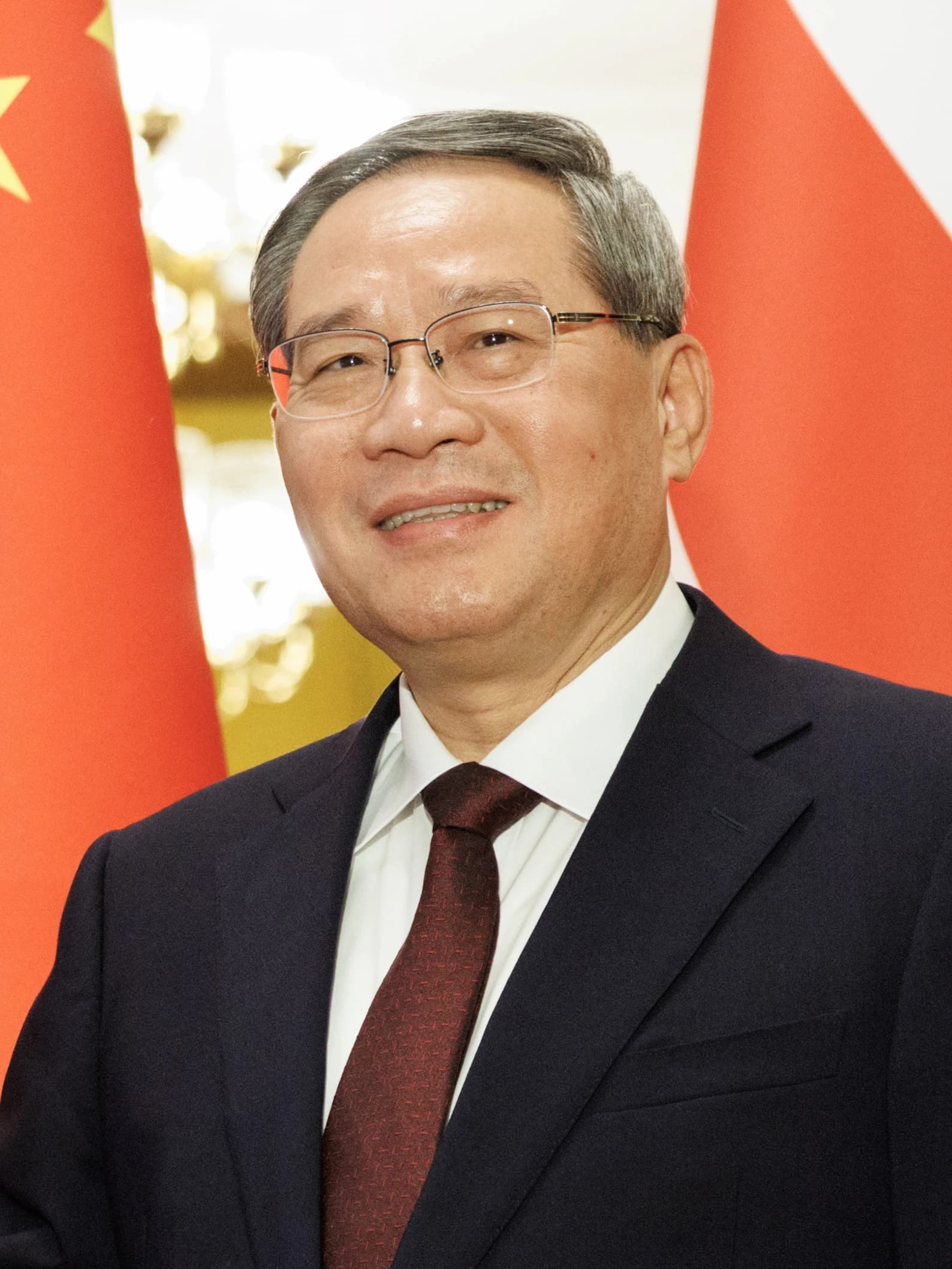 Li Qiang, Premier of China, stands for a portrait indoors with flags.
