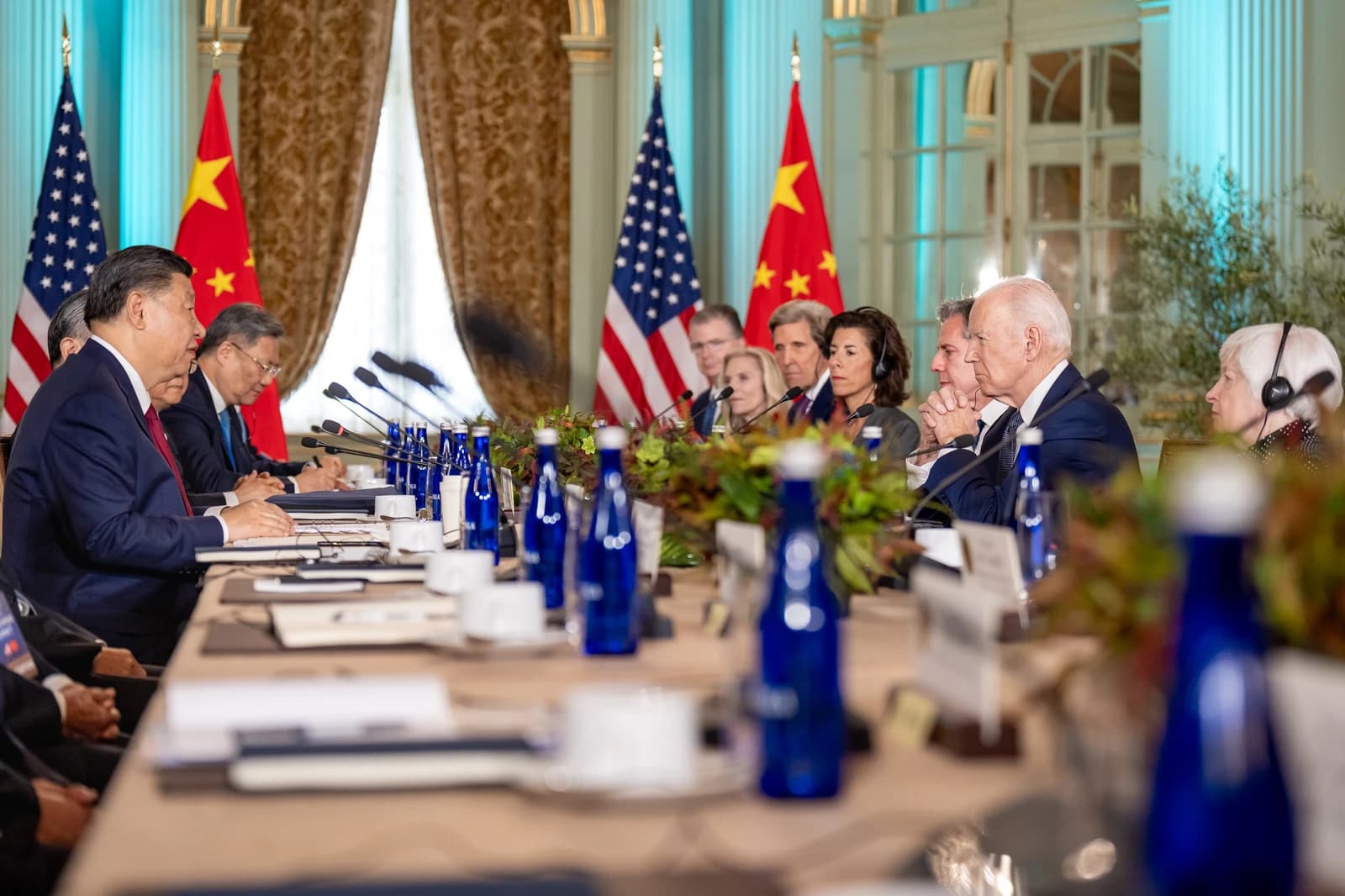 Xi Jinping and Joe Biden seated at a long table during a meeting with other officials.