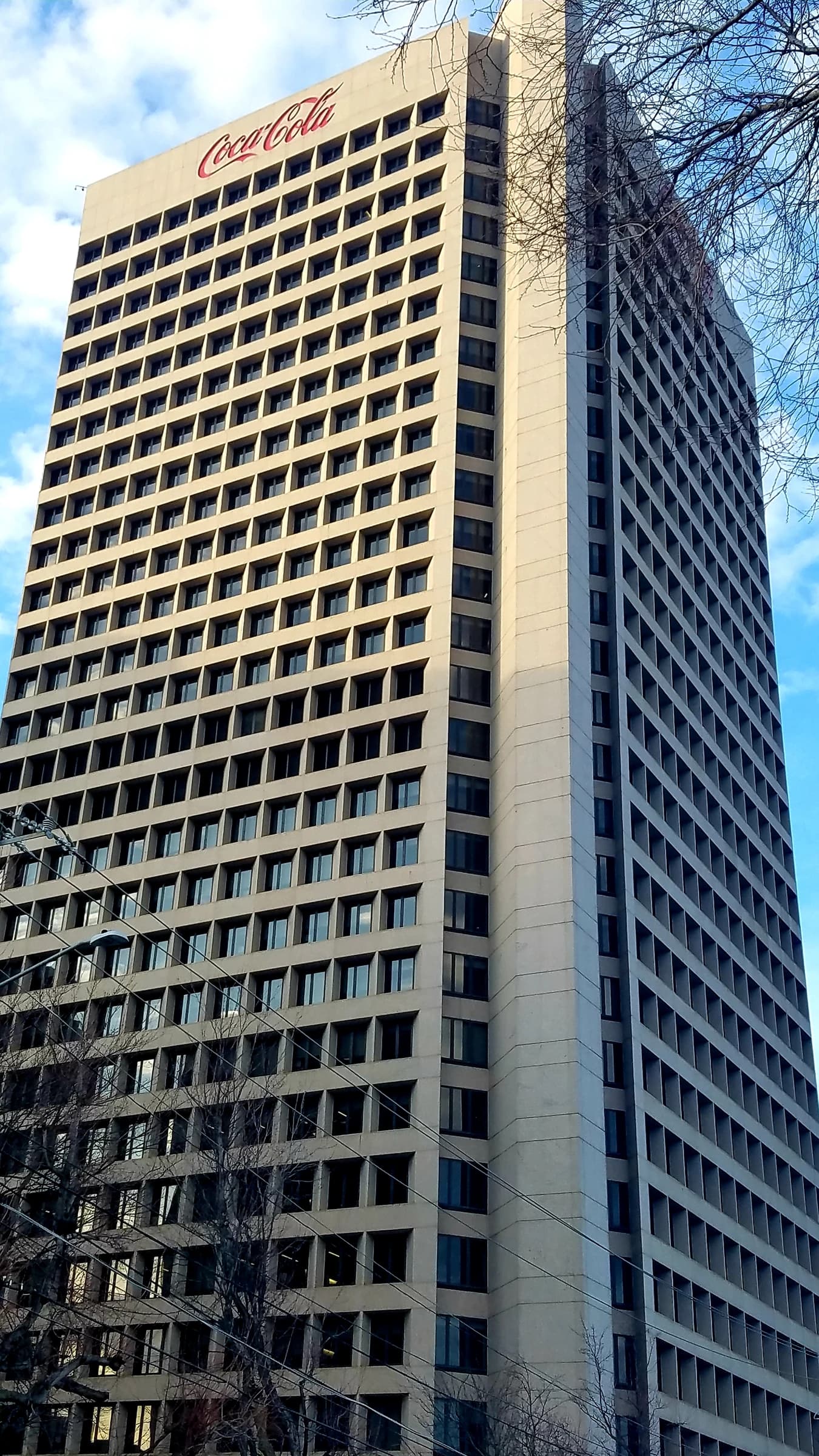 Coca-Cola World Headquarters building against a blue sky with some bare tree branches.