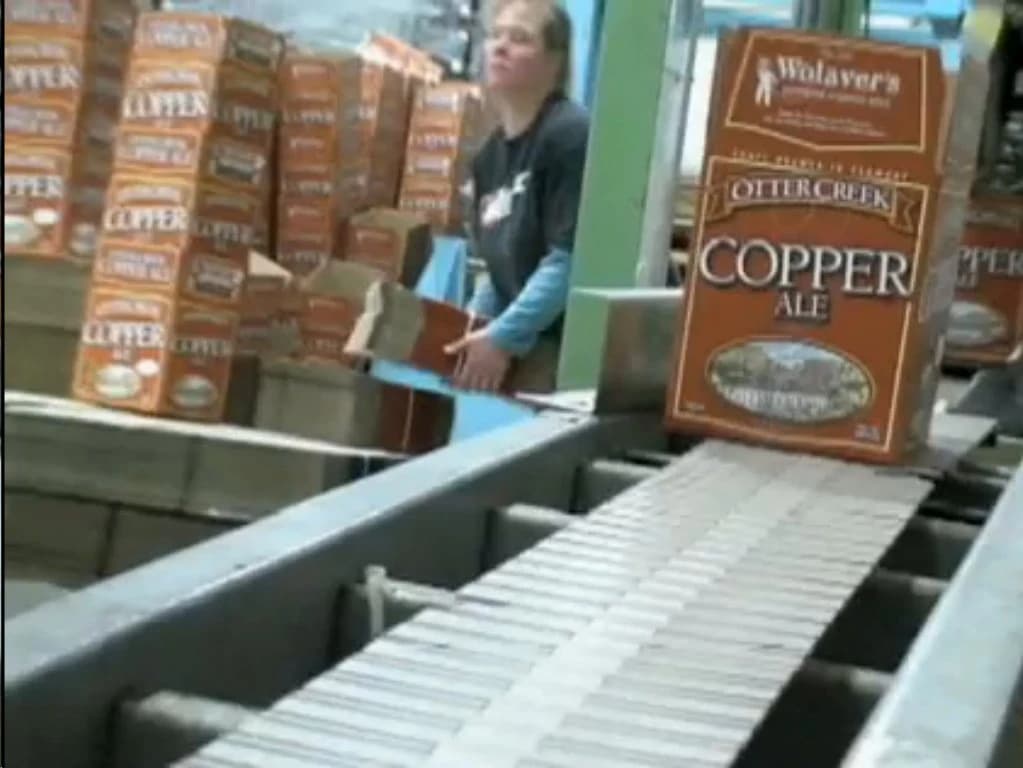 Brewery worker placing cases of Otter Creek Copper Ale beer onto a conveyor belt.