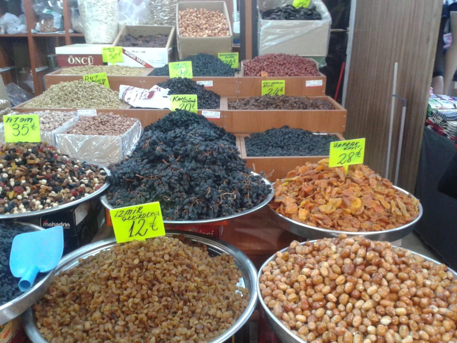 Various dried fruits and nuts, including raisins, in large metal bowls at a market.