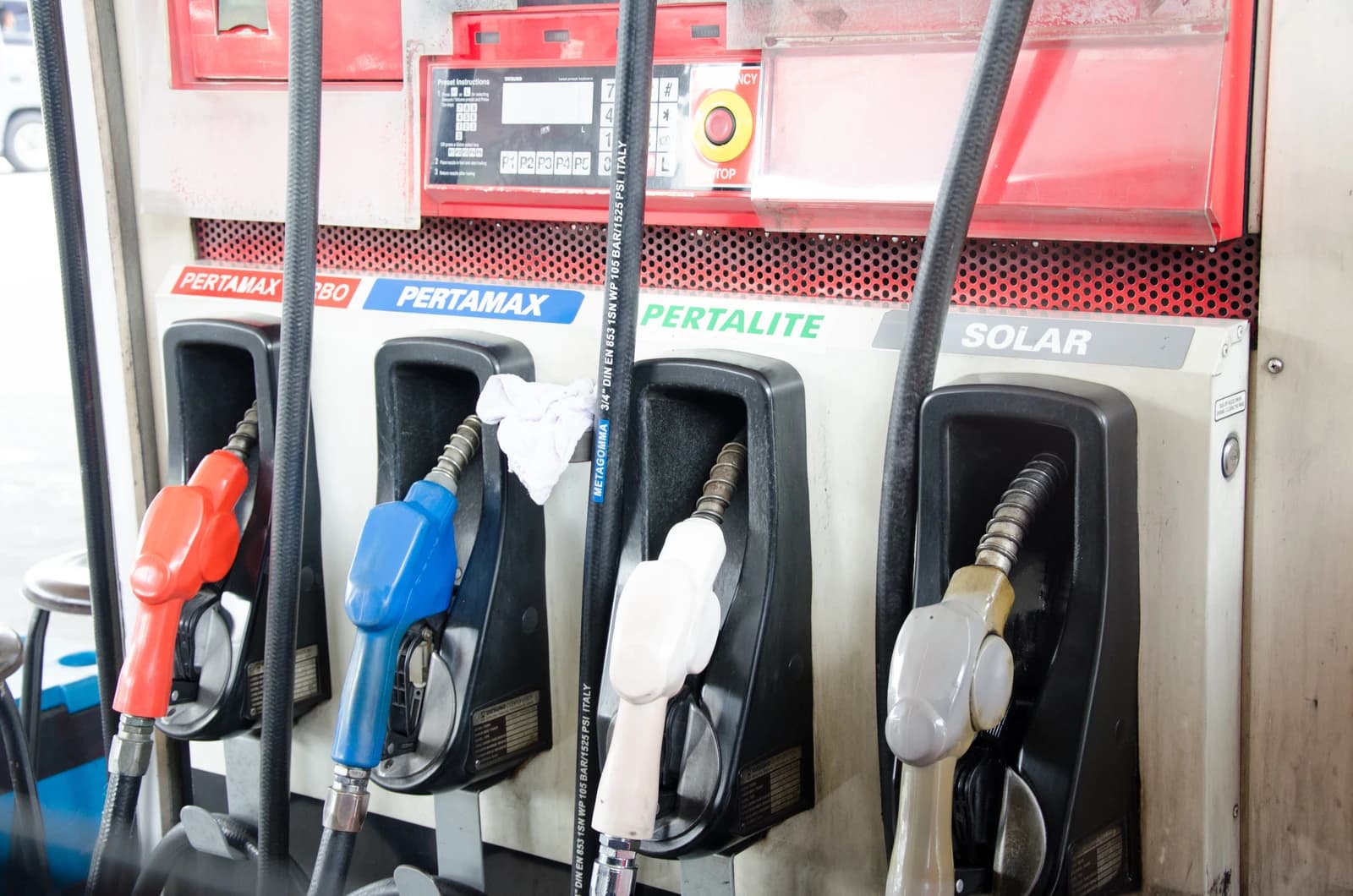 Multiple colored fuel nozzles are hanging from pumps at a gas station.