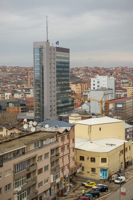 Overview of the city of Pristina, Kosovo, featuring various buildings under a cloudy sky.