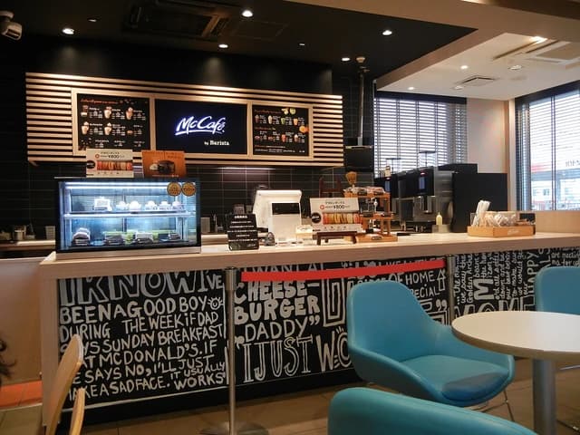 Interior view of a McDonald's McCafé featuring a service counter and tables with chairs.
