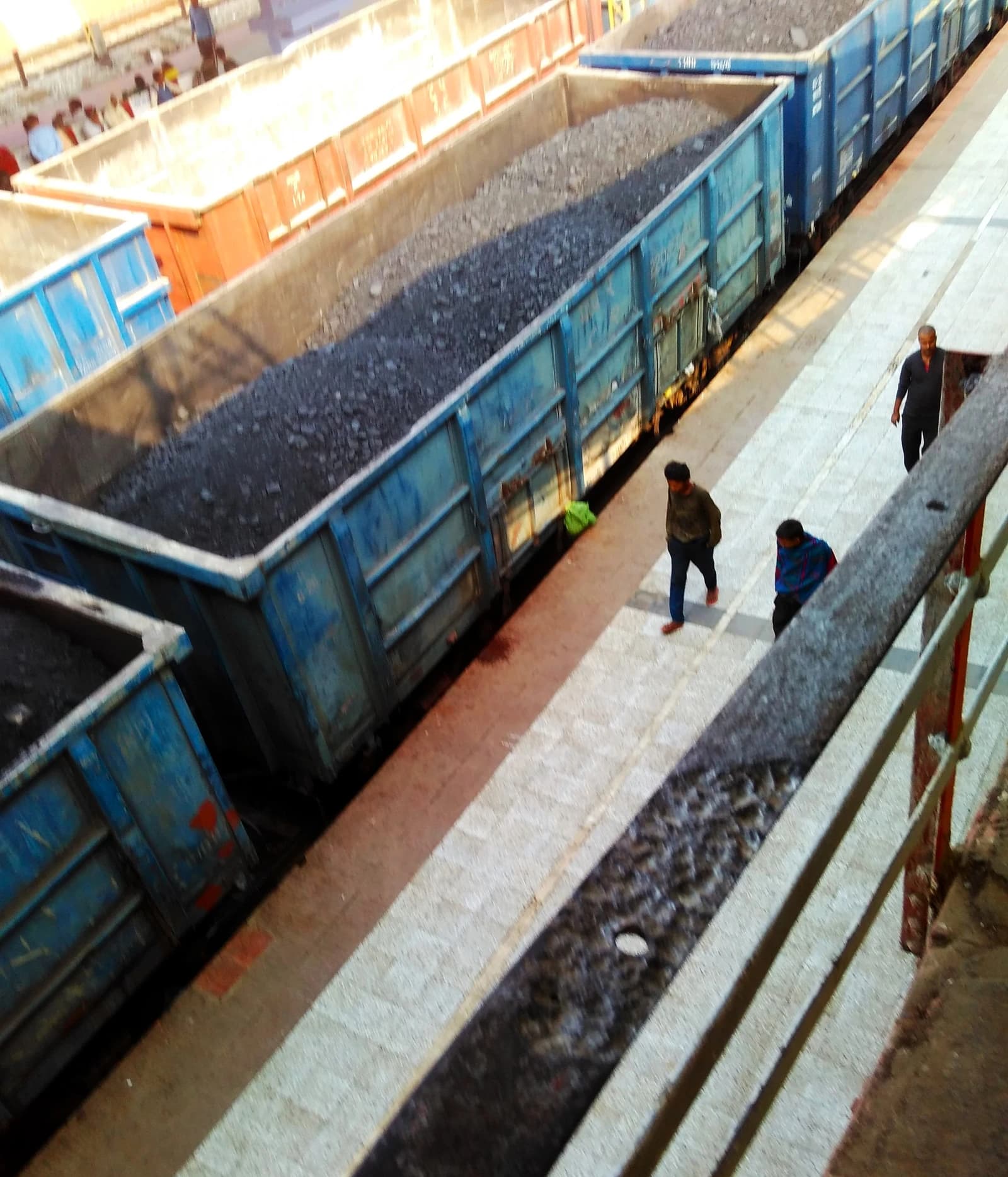 Coal loaded in blue and orange railway wagons at a station platform.
