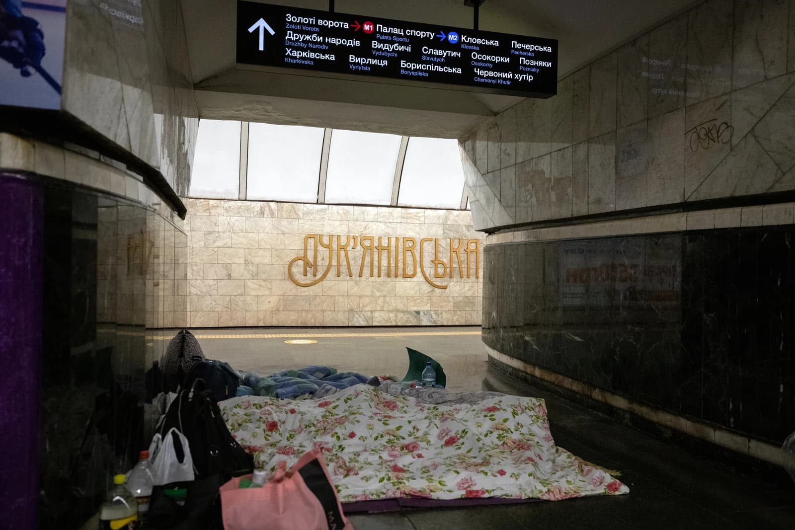 Makeshift sleeping area with blankets and bags on the floor of a Kyiv metro station.