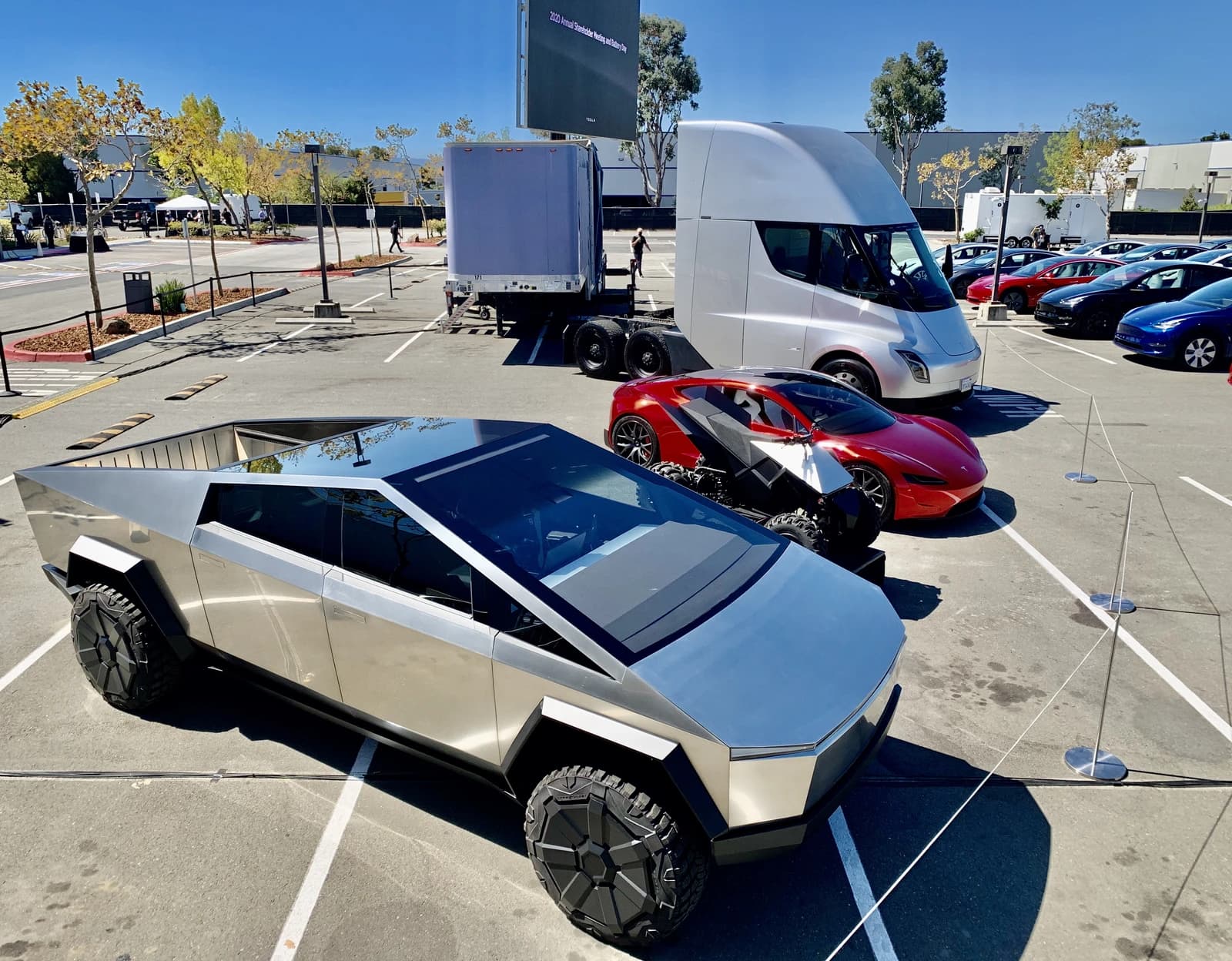 Tesla Cybertruck, Roadster, and Semi truck parked outdoors under a clear sky.