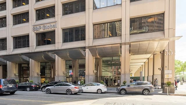Exterior view of the S&P Global corporate building with parked cars and people walking.